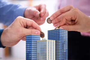 Mains plaçant des pièces de monnaie sur des maquettes de bâtiments pour illustrer l'investissement dans le crowdfunding immobilier.