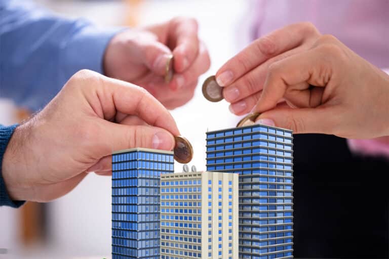 Mains plaçant des pièces de monnaie sur des maquettes de bâtiments pour illustrer l'investissement dans le crowdfunding immobilier.
