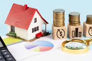 Modèle réduit de maison avec des piles de pièces et des blocs symbolisant la monnaie et les statistiques, mettant en évidence l'impact des taux d'intérêt sur l'immobilier.
