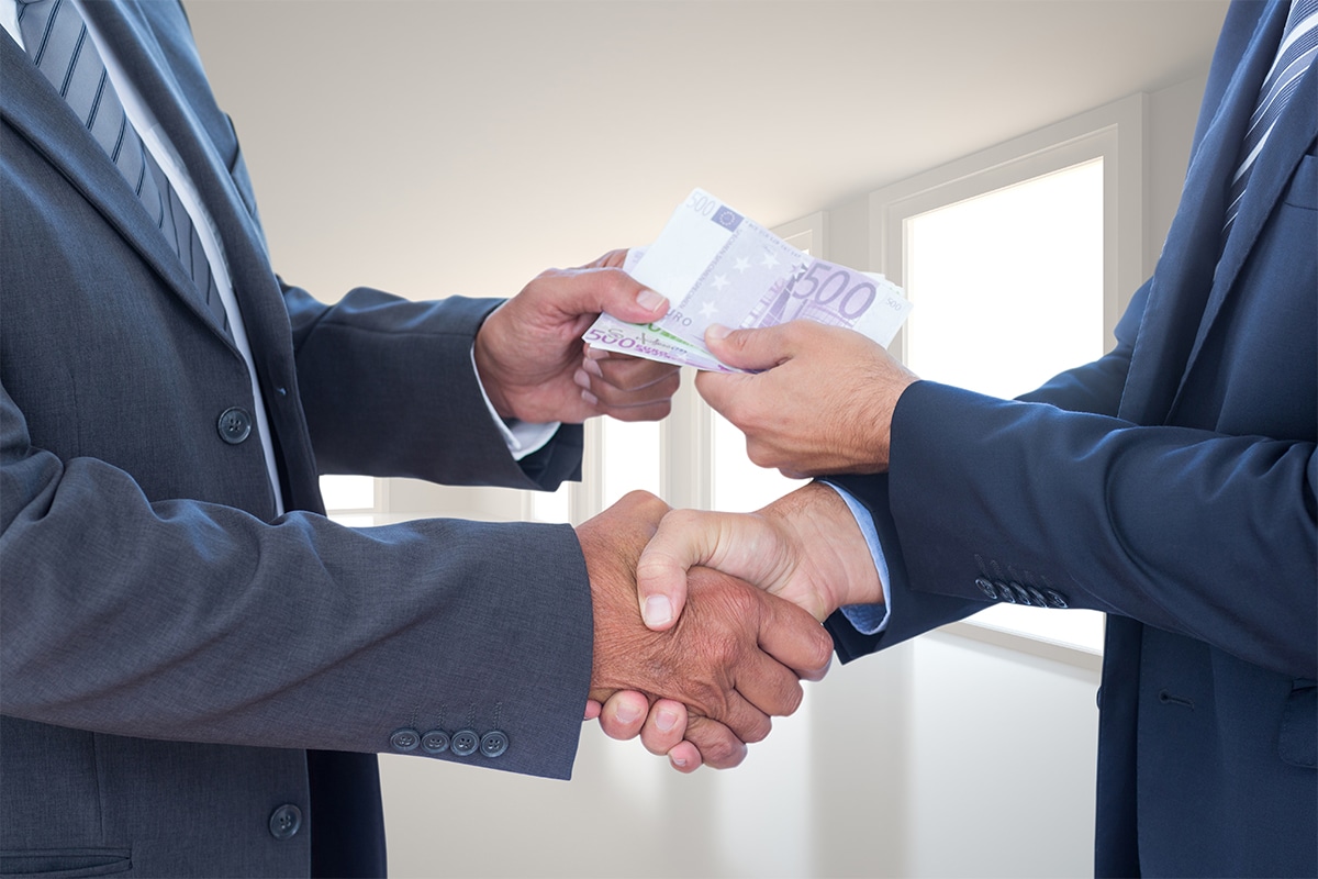 Deux hommes d'affaires se serrant la main, l'un remettant discrètement des billets de banque à l'autre, illustrant un prêt personnel sans garantie.