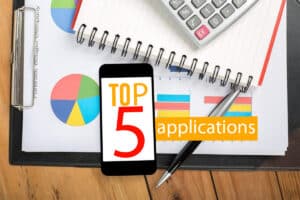 Smartphone affichant 'TOP 5 applications' posé sur un bureau avec un calculateur et des graphiques financiers, indiquant des outils de gestion de dépenses.