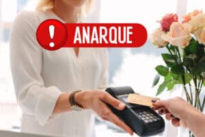 Femme passant une carte de crédit dans un terminal de paiement avec un avertissement « ANARQUE » en surimpression.