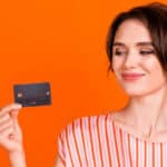 Femme souriante tenant une carte de crédit noire sur un fond orange.