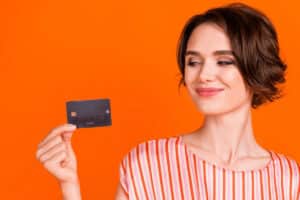 Femme souriante tenant une carte de crédit noire sur un fond orange.