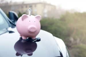 Une tirelire rose en forme de cochon avec un billet de banque sur le capot d'une voiture.