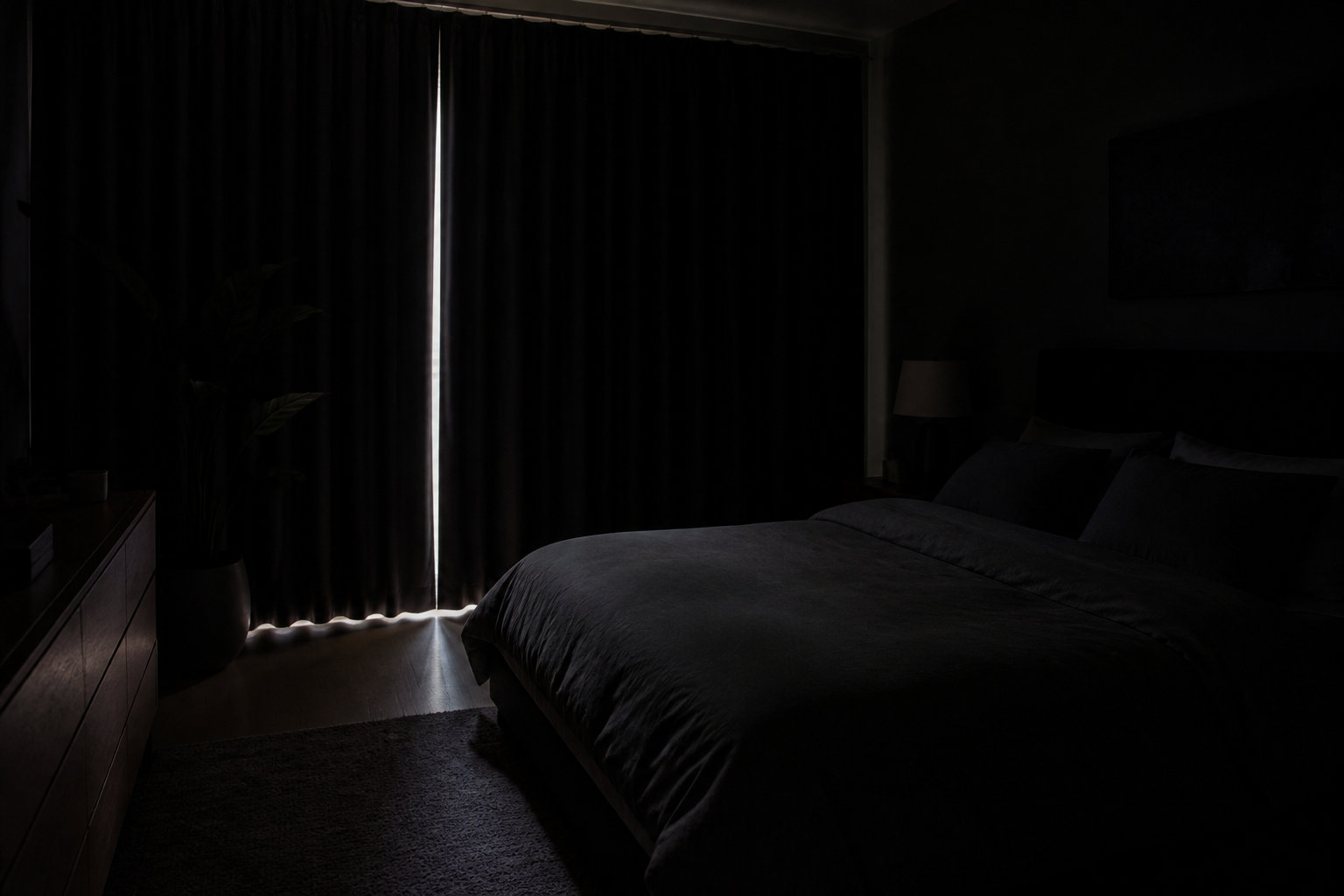 Chambre sombre avec un rai de lumière filtrant par des rideaux fermés, évoquant le sommeil en journée.
